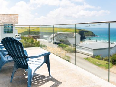 A balcony with two blue chairs overlooking houses a road and the sea at Blue Bay Beach House in Mawgan Porth