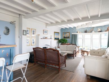A living room with wicker sofas a white leather sofa a fireplace blue door and windows at Blue Bay Beach House in Mawgan Porth