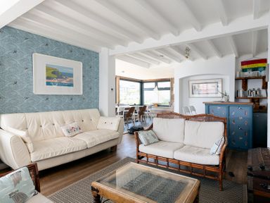 A living room with two sofas a glass coffee table and a dining area in the background at Blue Bay Beach House in Mawgan Porth