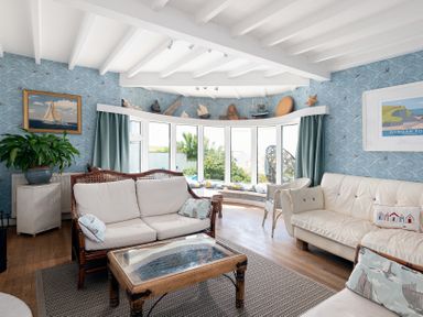 A living room with sofas a coffee table a bay window with cushions and nautical decorations at Blue Bay Beach House in Mawgan Porth