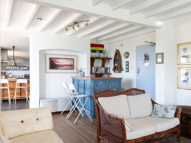 A living room with a blue bar counter white bar stools and a kitchen area in the background at Blue Bay Beach House in Mawgan Porth