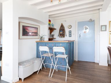 A kitchen area with a blue bar counter and two white stools near a light blue door at Blue Bay Beach House in Mawgan Porth