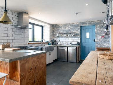A kitchen with wooden countertops a blue door and shelves with cups at Blue Bay Beach House in Mawgan Porth