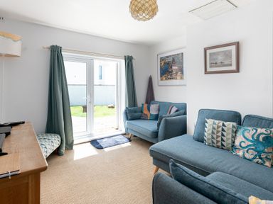A living room with blue sofas and sliding glass doors leading to a garden at Blue Bay Beach House in Mawgan Porth
