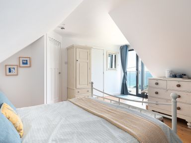 A bedroom with a bed a wardrobe a chest of drawers and a door leading outside with curtains at Blue Bay Beach House in Mawgan Porth