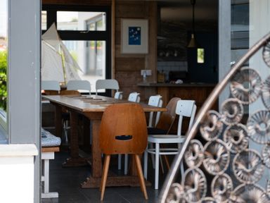 A dining area with a wooden table and mixed chairs at Blue Bay Beach House in Mawgan Porth