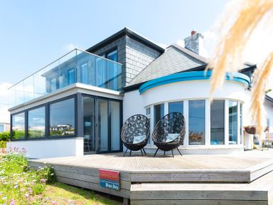 Modern house with large glass windows and a wooden deck with two black chairs at Blue Bay Beach House in Mawgan Porth