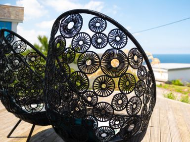 Two black circular woven chairs on a wooden deck with a view of the sea at Blue Bay Beach House in Mawgan Porth