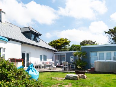 An outdoor area with seating including a sofa and chairs a hot tub and some plants at Blue Bay Beach House in Mawgan Porth