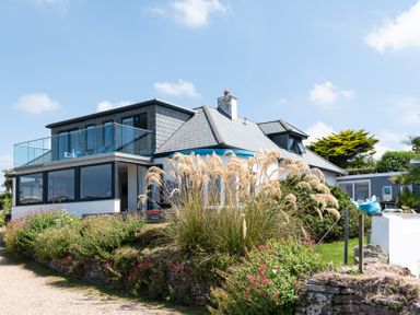 A house with a glass balcony and garden plants at Blue Bay Beach House in Mawgan Porth