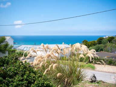 A coastal view with ornamental grasses and houses overlooking the ocean at Blue Bay Beach House in Mawgan Porth