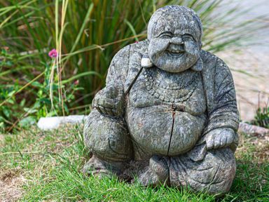 A stone statue of a laughing Buddha placed on grass with plants in the background at Blue Bay Beach House in Mawgan Porth