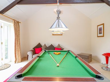 A room with a pool table with cues on it a sofa with cushions a red stool and curtains at Lambkin Cottage in St Columb Major