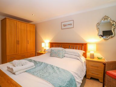 A bedroom with a wooden bed and wardrobe bedside tables with lamps and a decorative mirror at Lambkin Cottage in St Columb Major