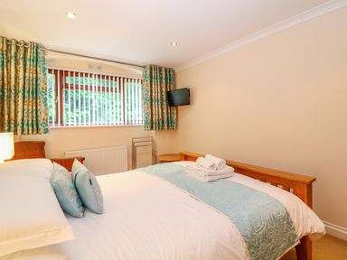 A bedroom with a wooden bed a window with patterned curtains and a wall-mounted tv at Lambkin Cottage in St Columb Major