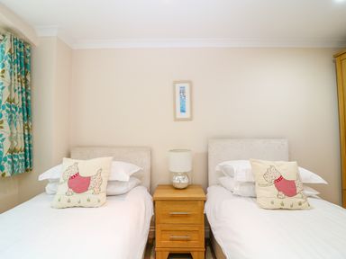 A bedroom with two single beds separated by a wooden nightstand with a lamp at Lambkin Cottage in St Columb Major