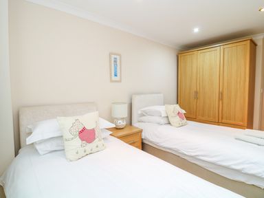 A bedroom with two single beds a nightstand with a lamp a wooden wardrobe and a small framed picture on the wall at Lambkin Cottage in St Columb Major