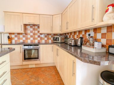 A kitchen with wooden cabinets a stainless steel oven and countertop appliances at Lambkin Cottage in St Columb Major