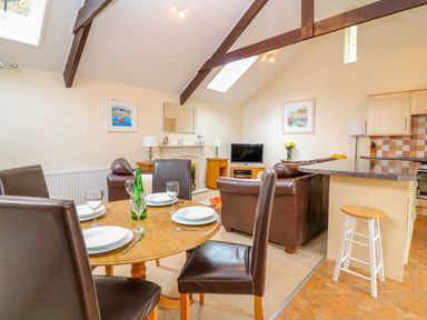 A dining table with plates and glasses near a living area with leather sofas and a television at Lambkin Cottage in St Columb Major