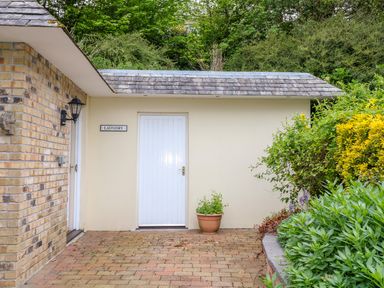 An outdoor area with a white door labeled laundry a brick wall light fixture a potted plant and greenery at Lambkin Cottage in St Columb Major