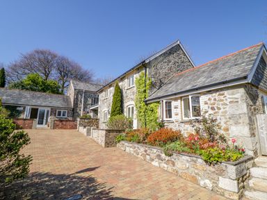 A stone house with a paved driveway and flower beds in front at Cornflower Cottage in St Columb Major