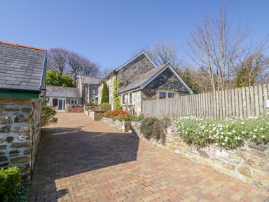 A driveway with stone cottages and a wooden fence with flowers at Cornflower Cottage in St Columb Major