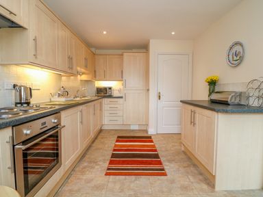 A kitchen with wooden cabinets a striped rug and countertop appliances at Cornflower Cottage in St Columb Major