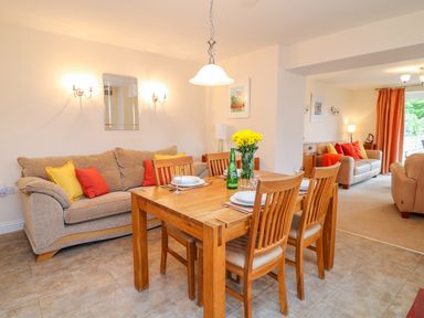 A dining area with a wooden table set for four and a sofa with colorful cushions at Cornflower Cottage in St Columb Major