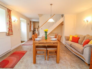 A dining area with wooden table and chairs set for six and a beige sofa with colorful cushions at Cornflower Cottage in St Columb Major
