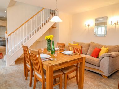 A dining area with wooden table and chairs near a staircase and a sofa with cushions at Cornflower Cottage in St Columb Major
