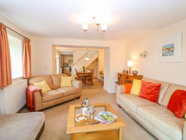 A living room with two beige sofas and a wooden coffee table with magazines and tea set at Cornflower Cottage in St Columb Major