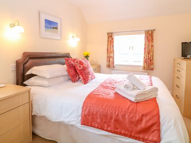 A bedroom with a bed red pillows folded towels bedside tables window with curtains at Cornflower Cottage in St Columb Major