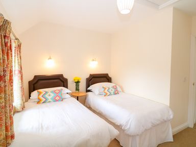 A bedroom with two single beds a small round table with flowers and patterned curtains at Cornflower Cottage in St Columb Major