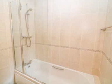 A bathroom with a bathtub shower and tiled walls at Cornflower Cottage in St Columb Major