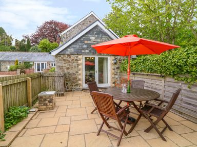 An outdoor patio with a round wooden table and chairs under an orange umbrella at Cornflower Cottage in St Columb Major