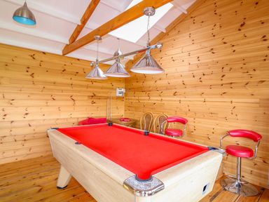 A room with a red pool table wooden walls two wicker chairs and two red bar stools at Cornflower Cottage in St Columb Major