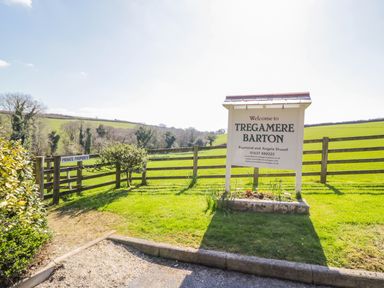A wooden sign welcoming to Tregamere Barton in a grassy area with a wooden fence and trees in the background