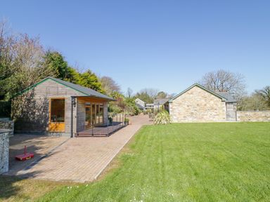 A grassy lawn with two small buildings and a paved walkway at Forget-me-not in St Columb Major