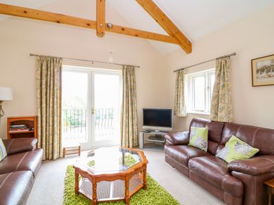 A living room with leather sofas a wooden coffee table a television and curtains at Forget-me-not in St Columb Major