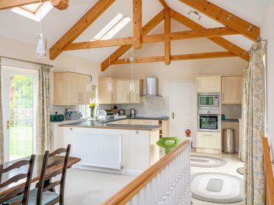 A kitchen with wooden beams windows curtains appliances and a dining table with chairs at Forget-me-not in St Columb Major