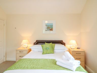 A bedroom with a bed green pillows and folded white towels on it with bedside tables and lamps at Forget-me-not in St Columb Major