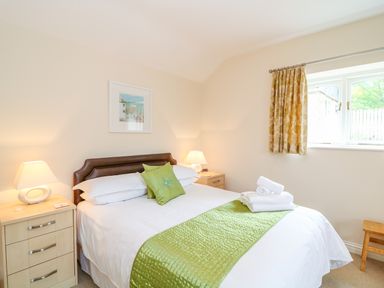 A bedroom with a bed green runner pillows bedside tables lamps window and curtains at Forget-me-not in St Columb Major