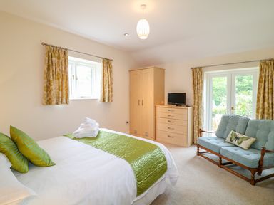 A bedroom with a bed folded towels wardrobe chest of drawers small tv and upholstered wooden framed sofa at Forget-me-not in St Columb Major