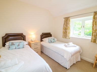 A bedroom with two single beds a nightstand with a lamp and a window with curtains at Forget-me-not in St Columb Major
