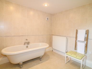 A bathroom with a freestanding bathtub a radiator and a small bench with towels at Forget-me-not in St Columb Major