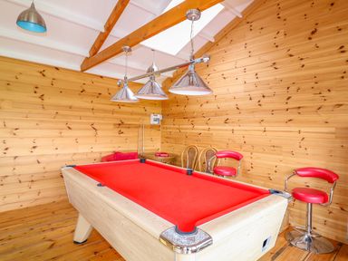 A game room with a red pool table two red bar stools and wooden walls at Forget-me-not in St Columb Major