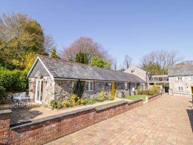 A stone cottage with a yellow door and a patio table with chairs on a paved area at FernGully in St Columb Major