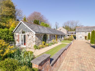 Stone houses with slate roofs and garden area along paved driveway at FernGully in St Columb Major