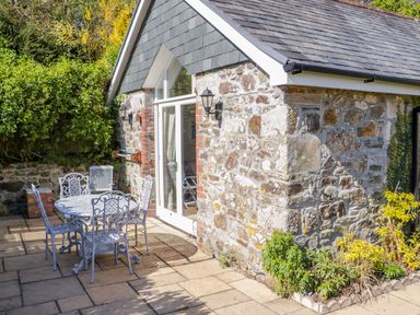A stone building with slate roof and glass door next to a patio table and chairs at FernGully in St Columb Major