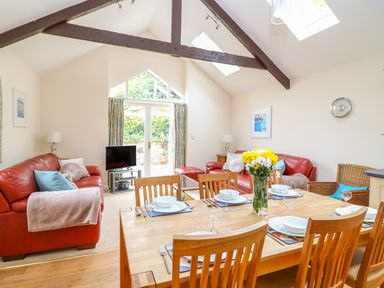 A dining table set with plates and glasses next to two red sofas in a living room with exposed beams at FernGully in St Columb Major